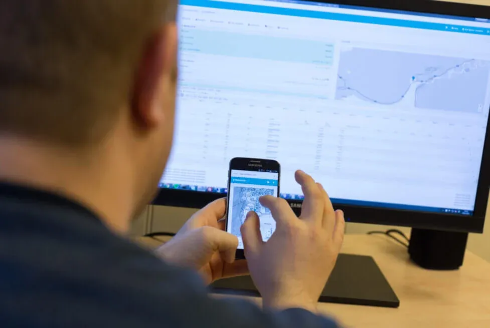 A person photographing a phone screen while using the Vendanor Connect management dashboard on a monitor.