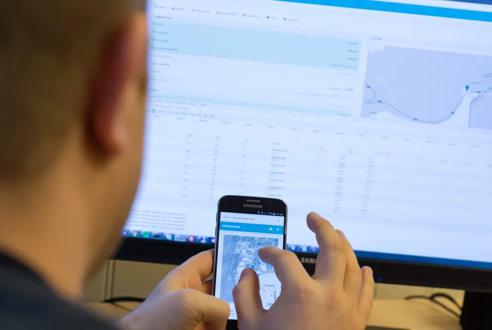 A person photographing a phone screen while viewing the Vendanor Connect management dashboard on a monitor.