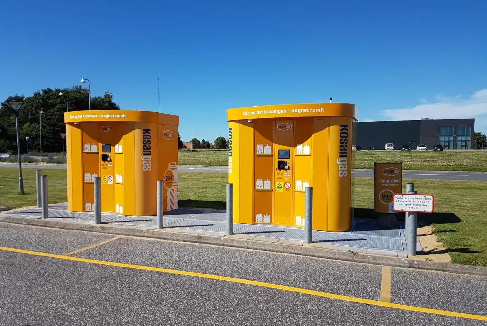 Two orange Kosangas Vendanor Propane Vending Machines installed at an outdoor site under a clear blue sky.
