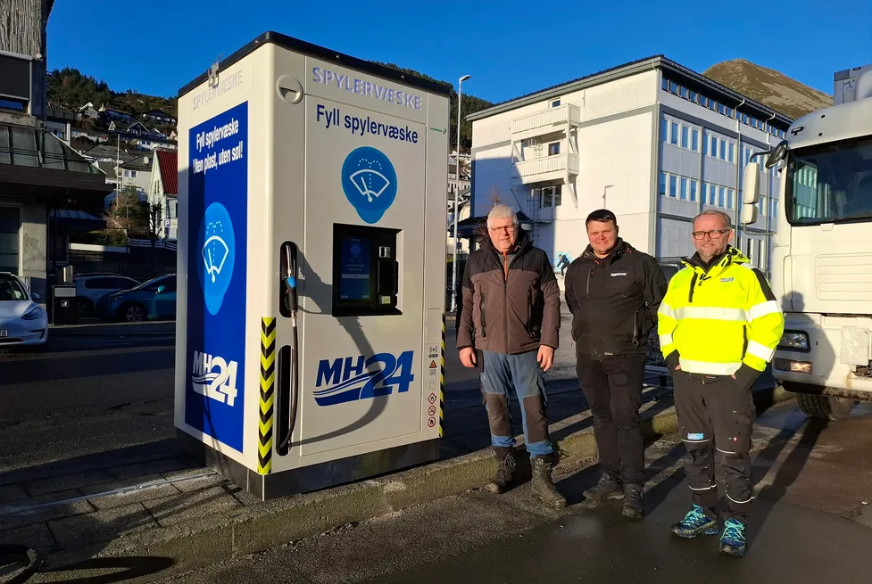 Three men standing beside an MH24-branded Vendanor Washer Fluid Dispenser on a street in Måløy.
