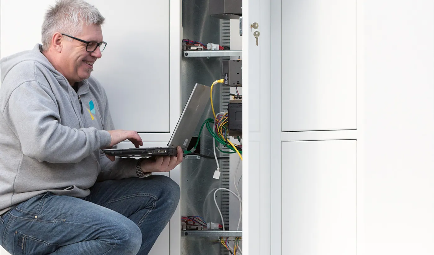 A Vendanor service technician with a laptop performing maintenance inside an open vending machine cabinet.