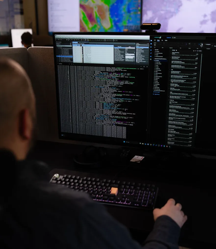 Vendanor support engineer working at dual monitors with code and system data in a darkened control room.